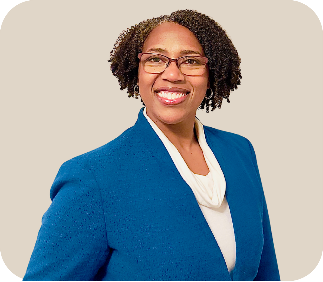 Woman who is smiling and wearing glasses, a blue blazer, and a white blouse.